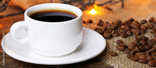 A white cup of coffee on a wooden background. Banner. Coffee beens on a linen fabric