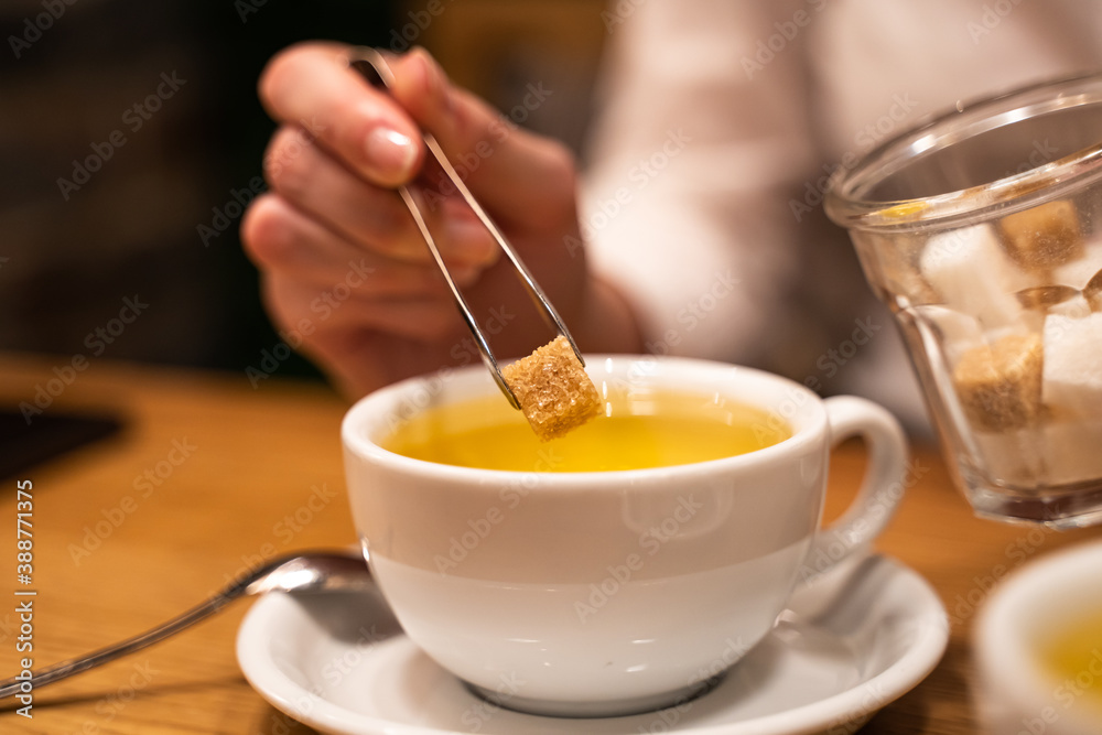 Close-up of a woman's hand throw brown sugar into a mug with tea. Close-up of a woman's hand throw brown sugar into a mug with tea.