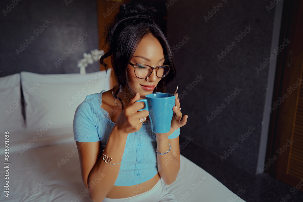 Beautiful Asian woman holding and drinking coffee on the bed in the morning in a hotel room