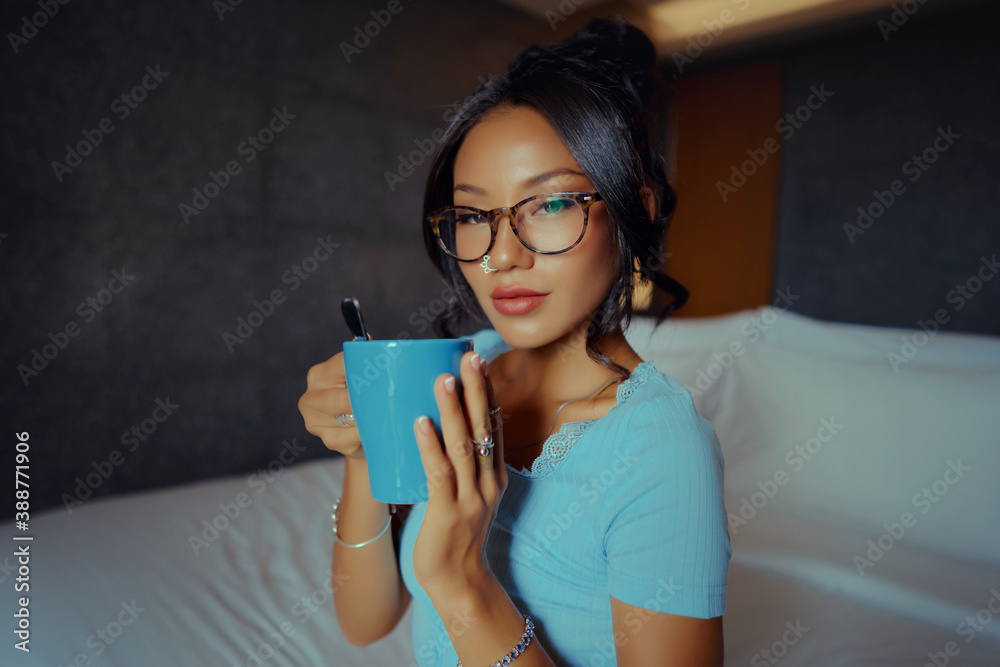 Beautiful Asian woman holding and drinking coffee on the bed in the morning in a hotel room