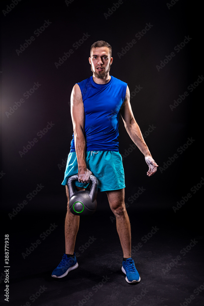 A sports man in a blue T-shirt and shorts holding a kettlebell on a black background. A sports man in a blue T-shirt and shorts holding a kettlebell on a black background.