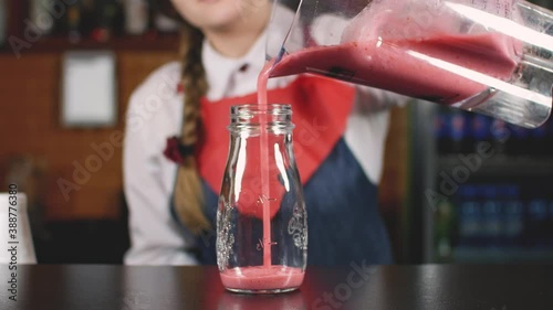 Girl bartender pours berry smoothie into a glass. Bar counter. Bartender's hands.