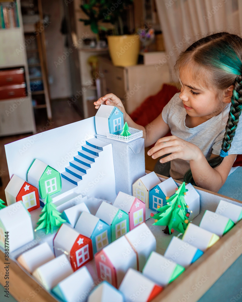 Origami advent calendar. Girl looking upon tiny paper houses, Christmas craft village Origami advent calendar. Girl looking upon tiny paper houses, Christmas craft village