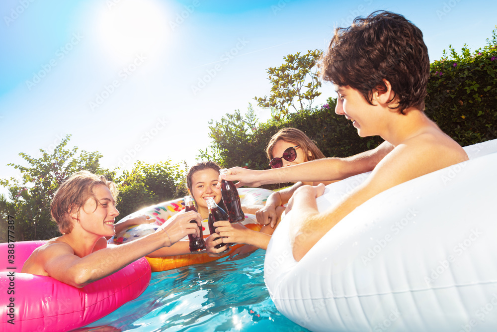Group of children party in the swimming pool drink soda from bottles