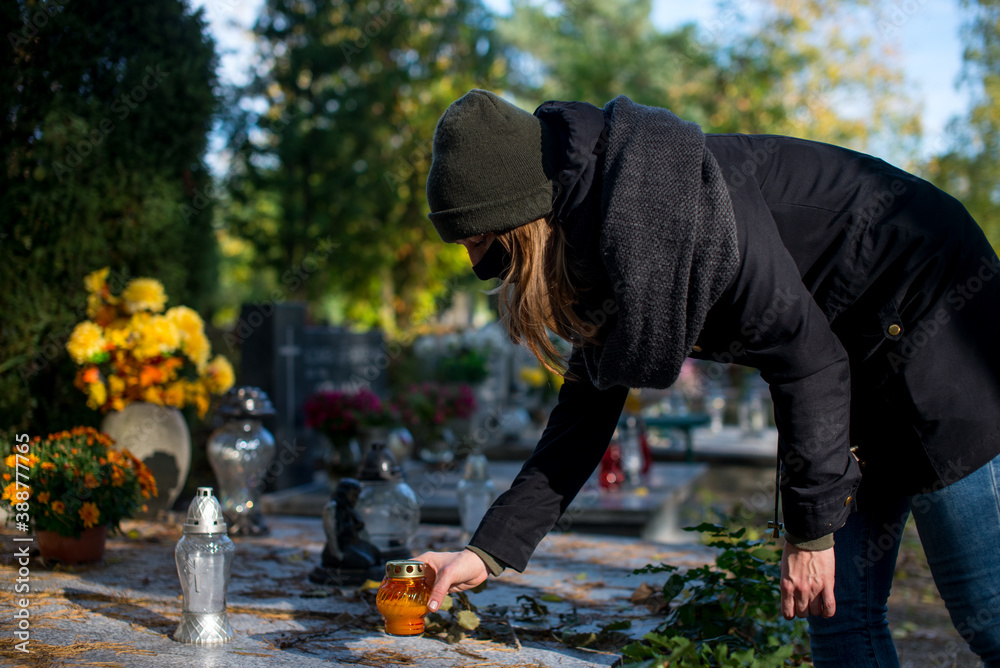 Ταπετσαρία A woman wearing a protective mask against the coronavirus in the cemetery, holding a candle snitch in a hand