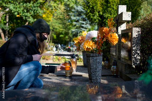 Photography A woman wearing a protective mask against the coronavirus in the cemetery, holding a candle snitch in a hand