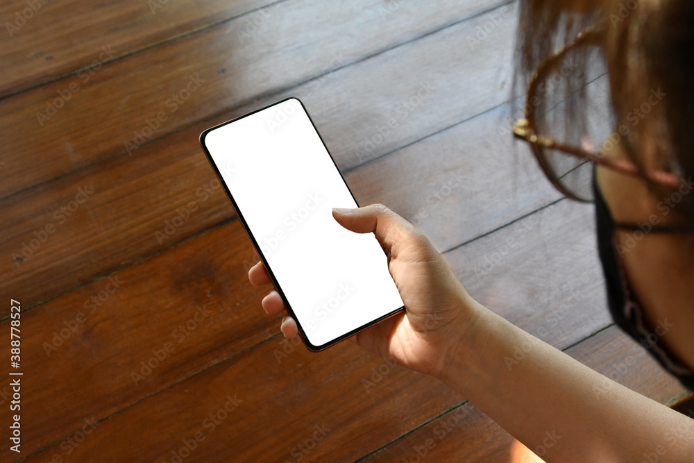 An Asian woman's hand wearing glasses holds a phone with a isolate screen in the room. An Asian woman's hand wearing glasses holds a phone with a isolate screen in the room.