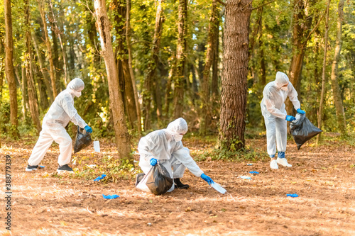 Workers in protective suit with face masks, collects dirty medical protections for covid-19 in a park photo