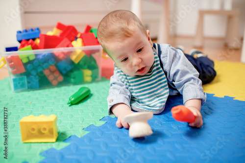 Little baby boy playing with colorful toys on the floor at home