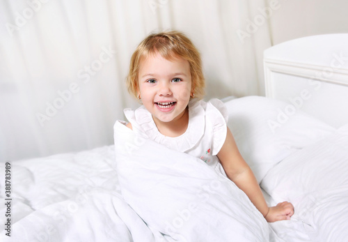 Child girl in bed smiling face..Toddler morning wake up.Caucasian little kid portrait.