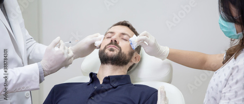 Young man getting beauty facial injections in salon. Beautician makes cosmetic injection into the male patient face. Beauty injections, mesotherapy, revitalization and rejuvenation concept