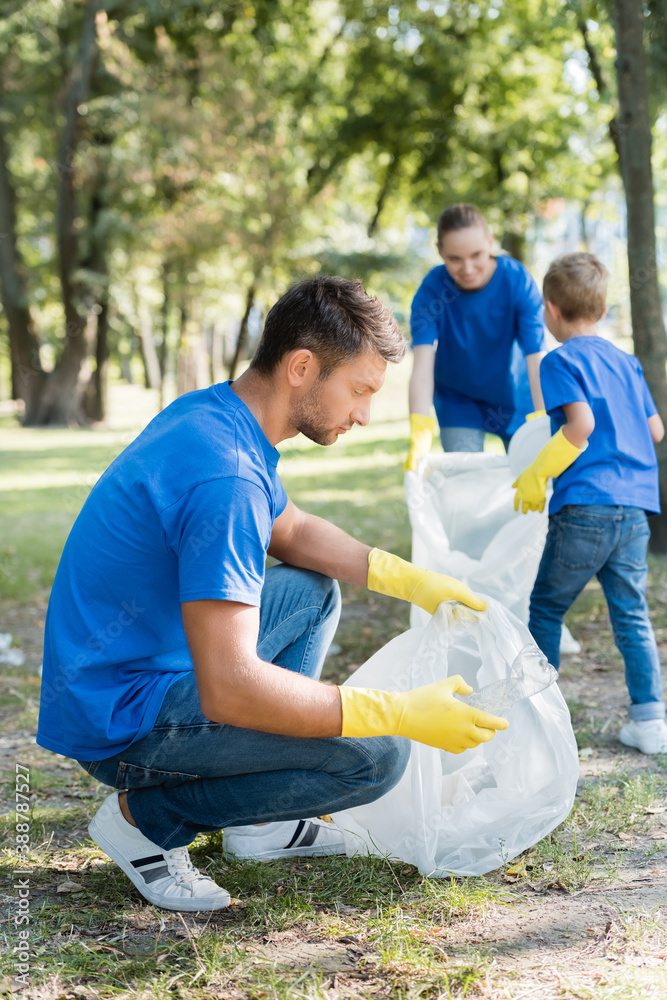 man holding recycled bag while family collecting rubbish on blurred background, ecology concept man holding recycled bag while family collecting rubbish on blurred background, ecology concept