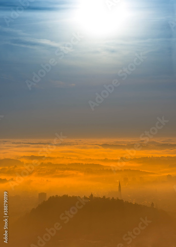 Amazing foggy sunrise over the city of Graz with Schlossberg hill and Church of the Sacred Heart of Jesus tower, in Styria region, Austria. Panoramic view from Plabutsch mountain on autumn morning.