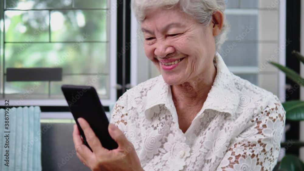 Smiling senior adult grandmother using smartphone sitting on sofa. Happy 70s elder woman holds mobile phone texting message, checking app, reading news at home. Smiling senior adult grandmother using smartphone sitting on sofa. Happy 70s elder woman holds mobile phone texting message, checking app, reading news at home.