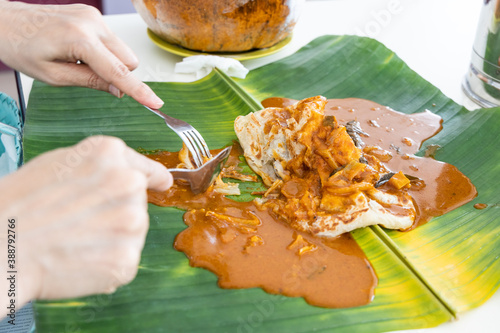 Photography Person eating roti canai or paratha served with curry served on banana leaf