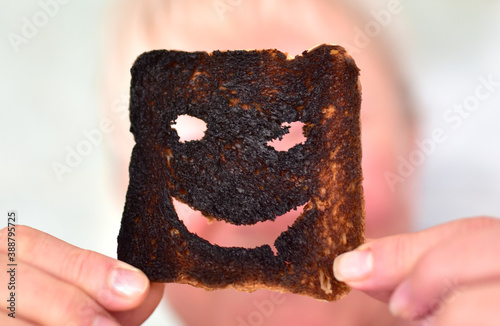 Burnt toast bread slices. Woman holds in hands a burnt slice of toast with an angry face expressing the emotion of sadness or sarcasm. Unsuccessful сooking breakfast before a work day or weekend