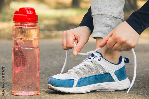 The girl ties the laces of her sneakers. Sports shoes and sports bottle close up