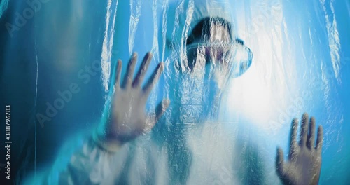 Medico o infermiere con tuta bianco covid si mette le mani in testa dalla disperazione dietro a un telo di plastica trasparente in ospedale. photo