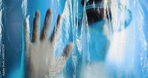 Medico o infermiere con tuta bianco covid si mette le mani in testa dalla disperazione dietro a un telo di plastica trasparente in ospedale. photo