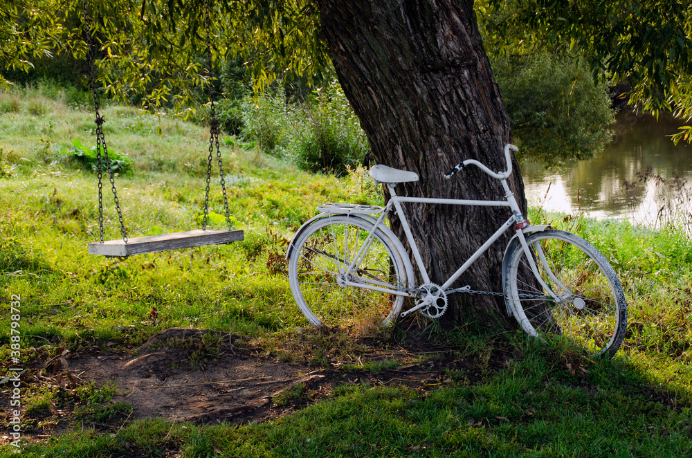 An old white Bicycle and a chain swing. Rest under a tree in a summer Park. An old white Bicycle and a chain swing. Rest under a tree in a summer Park.