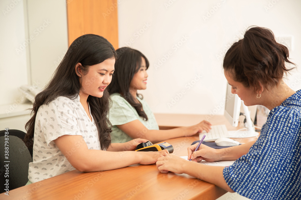Female customer filling information in the check-in form at the counter with receptionist. Woman client signing document in office by the desk Female customer filling information in the check-in form at the counter with receptionist. Woman client signing document in office by the desk