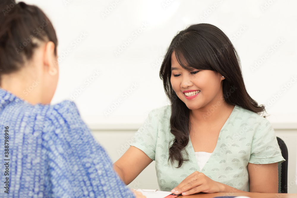 Smiling asian manager, advisor or hotel representative talking with client customer sitting by the desk Smiling asian manager, advisor or hotel representative talking with client customer sitting by the desk