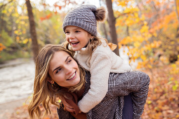 Little girl and her mother playing in the autumn park with child on back