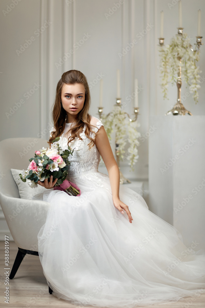 Gorgeous amazing bride with flower bouquet sitting on armchair in white studio interior Gorgeous amazing bride with flower bouquet sitting on armchair in white studio interior