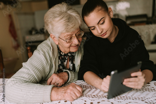 A teenage caucasian granddaughter shows her senior grandmother how to use a tablet. Education about new technology