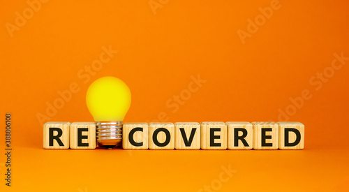 Wooden cubes with word 'recovered'. Yellow light bulb. Beautiful orange background. Business concept. Copy space. photo