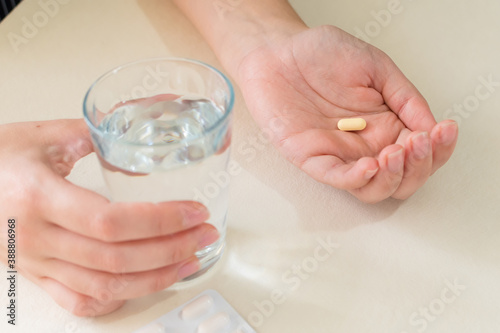 Yellow pill and a glass of water in female hands, on desk. health concept