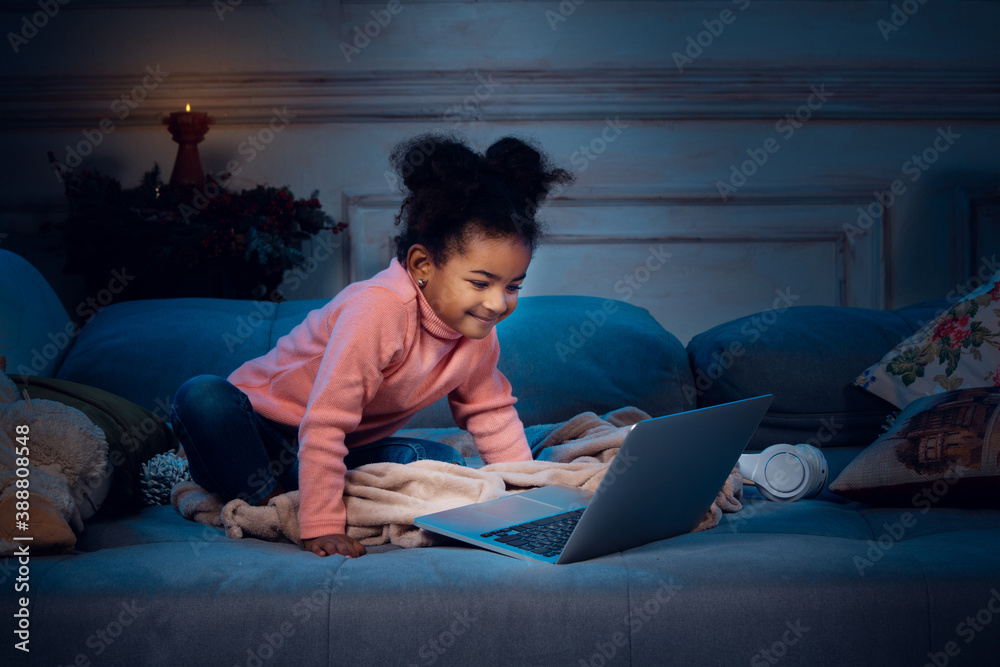 Happy african-american little girl during video call with laptop and home devices, looks delighted and happy. Talking to Santa before New Year's eve, her family, taking online preschool class. Happy african-american little girl during video call with laptop and home devices, looks delighted and happy. Talking to Santa before New Year's eve, her family, taking online preschool class.