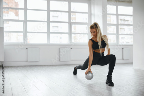 A pretty fit young woman doing frontal lunges or squats indoors. The blonde is engaged in the morning at dawn in the white room. Healthy lifestyle