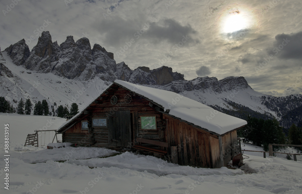 Eine verschneite Holzhütte vor winterliche Gipfel der Geislerspitzen in Südtirol