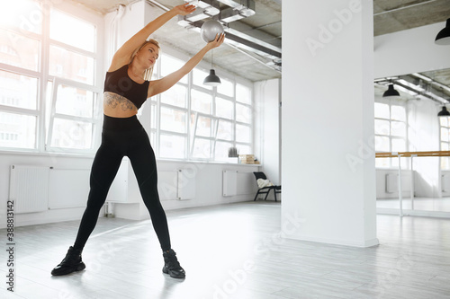 blonde is engaged in the gym. A young sportswoman in a black suit is doing stretching while standing in a white gym. gymnastics. holding a ball