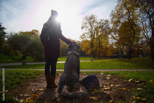 Młoda kobieta trzymająca rękę na pomniku psa w parku.  © Rafal