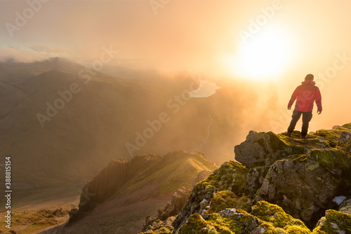 Lone hiker wearing red coat on mountain top with misty dramatic view. Taken in the Lake District  UK.
