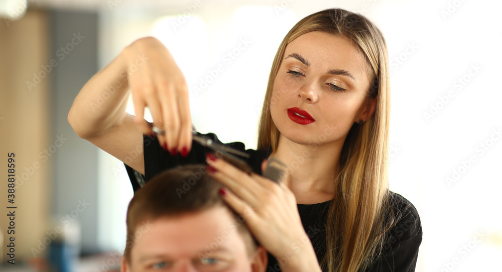 Fototapeta premium Female Hairstylist Cutting Hair of Man Client. Woman Hairdresser Holding Scissors in Hand. Young Stylist Making Haircut for Male Customer. Guy Getting Hairdo in Beauty Salon. Beautician Styling Hair