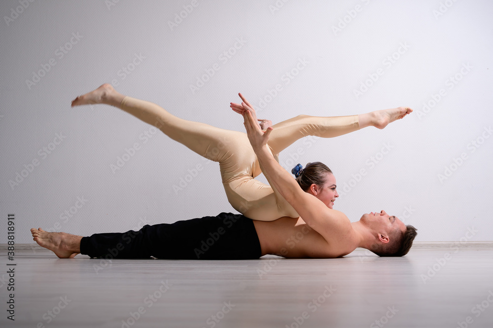 Obraz premium A duet of acrobats showing a pair trick. A woman in gymnastics overalls in a handstand over a shirtless man lies on his back. Very flexible circus performers.