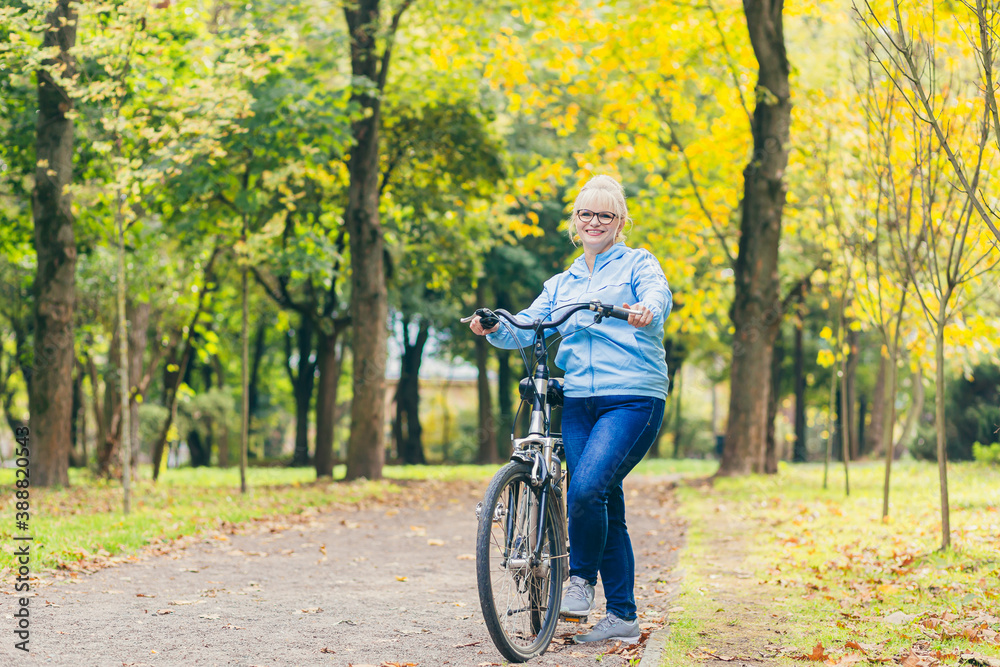 senior woman walking in the park with a bicycle, sunny day