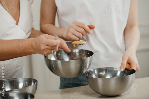 A close photo of the hands of two women, one of them is moving the yolk in a spoon to another stainless steel soup bowl in the kitchen.