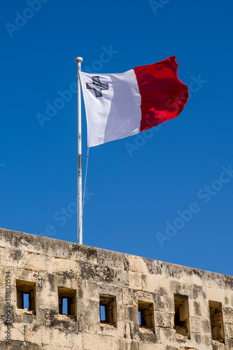 A Maltese Flag flies over the Island's Capital City of Valletta against a plain blue sky