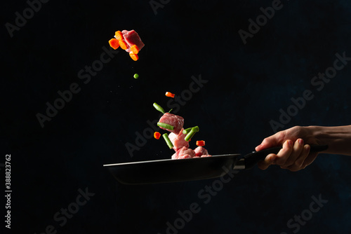 Chef hand tossed chopped pork or beef with mix of vegetables in frying pan on black background. Backstage of cooking grilled meat for dinner. Food concept. Frozen motion. Traditional asian cuisine.