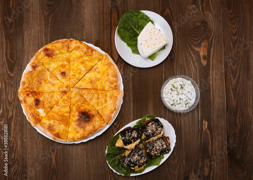 Baked homemade cheese pie, cheese, cheese sauce and eggplant salad on wooden background. Bulgarian banitsa, Georgian khachapuri, Greek tiropita photo