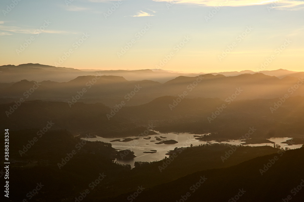 Bright golden sunlight in morning. Horizon over mountain range with stunning sunrise orange light. Maskeliya reservoir in valley. Panoramic view from Adam's Peak mountain (Sri Pada). Sri Lanka