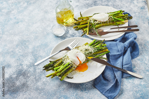 Green asparagus with poached egg and parmesan, vegetarian breakfast served on two white plate on light background.