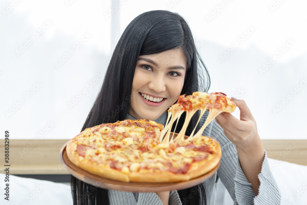 Beautiful happy smiling girl sitting on the bed showing a whole pizza ...