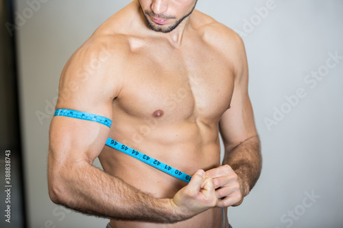 athletic man measures his bicep with a measuring tape
