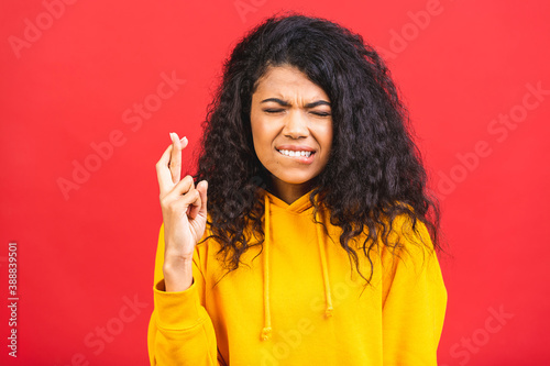 Black african american girl crossing fingers for good luck, winning lottery expectation, hope islated over red background.