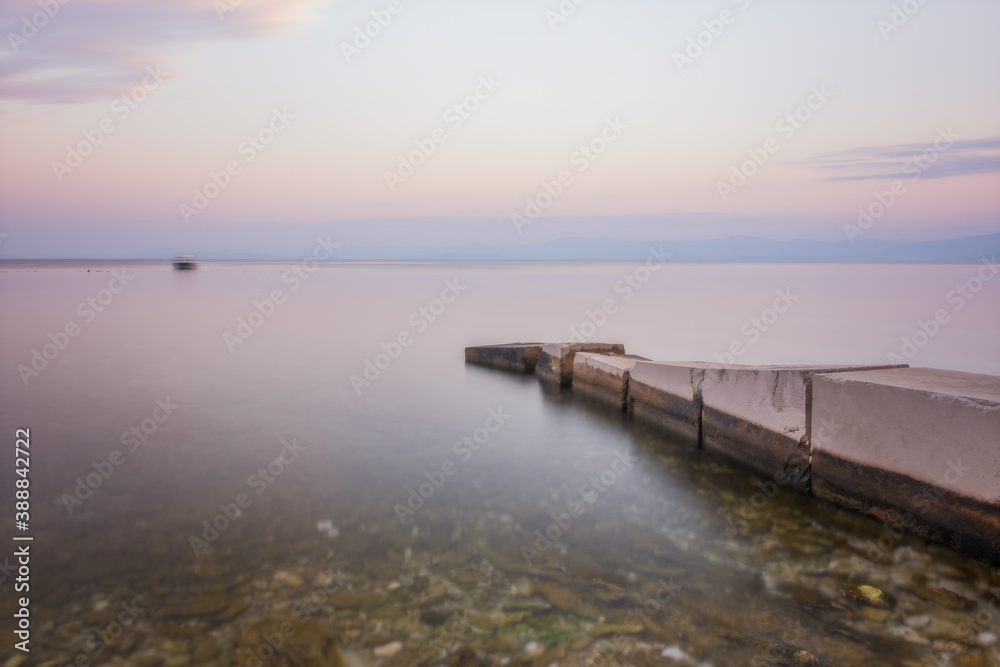Stone pier with a boat in long exposure, low saturation. Croatia, Brac island, Supetar at sunrise. August 2020
